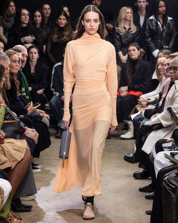 Model Walking in Proenza Schouler Fall Winter 2024 Runway Show Wearing Paula Dress in Blush Sheer Crepe Jersey, Stiltsman Stirrup in Black Compact Jersey, Silo Bag in Grey Embossed Ostrich Calf, and Tee Toe Ring Sandal in Black Nappa
