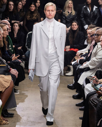 Model Walking in Proenza Schouler Fall Winter 2024 Runway Show Wearing Archer Jacket in Smoke Wool Twill, Rio Top in Bone Tulle Jersey, Demi Shirt in Bone Silk Viscose, Teddy Pant in Smoke Wool Twill, Flip Shoulder Bag in Light Grey Nappa, and Tee Over the Knee Boots in Black Viscose Knit