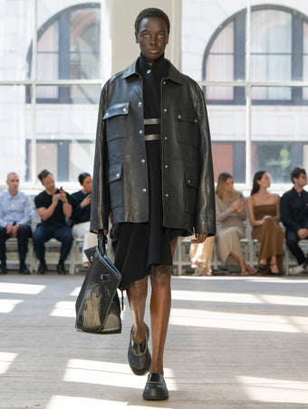 Image of model walking Proenza Schouler SS25 Runway wearing Reinhardt Dress in Wool Cashmere Knit in Black and Brice Jacket in Grainy Leather in Black and Days Carryall in Black Mesh in BLACK and Box Bag in Manilla Croc Embossed Calf in MANILLA and Silo Bag in Optic White Eyelet Covered Nappa in OPTIC WHITE and Caribou Mule in Black