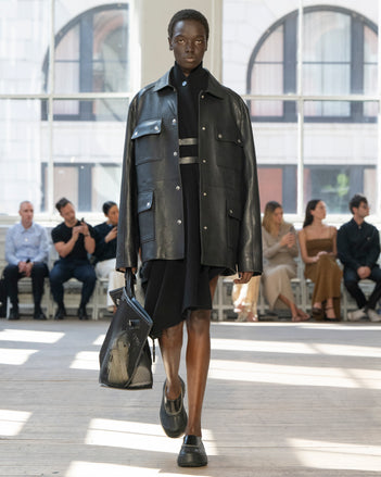 Image of model walking Proenza Schouler SS25 Runway wearing Reinhardt Dress in Wool Cashmere Knit in Black and Brice Jacket in Grainy Leather in Black and Days Carryall in Black Mesh in BLACK and Box Bag in Manilla Croc Embossed Calf in MANILLA and Silo Bag in Optic White Eyelet Covered Nappa in OPTIC WHITE and Caribou Mule in Black