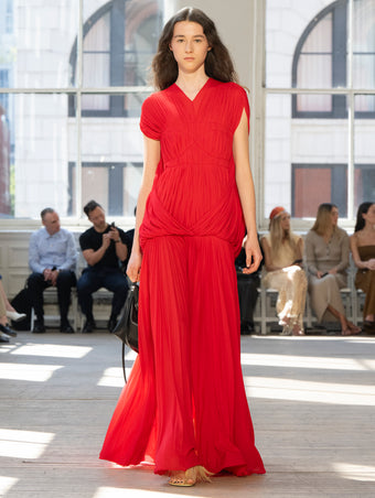 Image of model walking Proenza Schouler SS25 Runway wearing Rumi Dress in Pleated Jersey in Scarlet and Tetra Shoulder Bag in Black Nappa in BLACK and Tee Feather Thong Sandal in RESIN