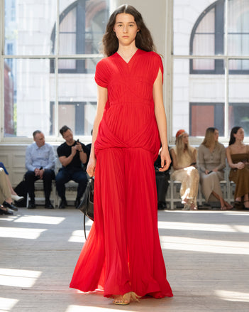 Image of model walking Proenza Schouler SS25 Runway wearing Rumi Dress in Pleated Jersey in Scarlet and Tetra Shoulder Bag in Black Nappa in BLACK and Tee Feather Thong Sandal in RESIN