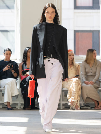 Image of model walking Proenza Schouler SS25 Runway wearing Keny Jacket in Wool Gabardine in Black and Ondine Top in Garment Printed Silk Viscose in Black and Oliver Pant in Wool Gabardine in Lilac and Silo Bag in Ruby Soft Hair Calf in RUBY and Glove Shoe in WHITE