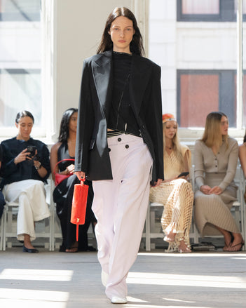 Image of model walking Proenza Schouler SS25 Runway wearing Keny Jacket in Wool Gabardine in Black and Ondine Top in Garment Printed Silk Viscose in Black and Oliver Pant in Wool Gabardine in Lilac and Silo Bag in Ruby Soft Hair Calf in RUBY and Glove Shoe in WHITE
