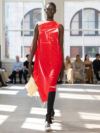 Image of model walking Proenza Schouler SS25 Runway wearing Ondine Dress in Garment Printed Silk Viscose in Crimson and Zip Legging in Technical Jersey in Black and Tetra Shoulder Bag in Manilla Nappa in MANILLA and Slash Slingback Pump in WHITE