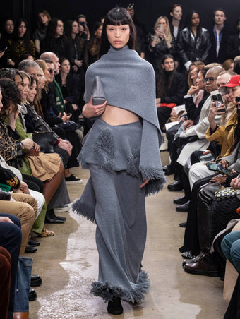 Model Walking in Proenza Schouler Fall Winter 2024 Runway Show Wearing Toni Dress in Ash Grey Textured Boucle Knit, Blanket in Ash Grey Textured Boucle Knit, Thin Belt in Black Nappa, Bond Bag in Light Grey Embossed Ostrich Calf, and Tee Over the Knee Boots in Black Viscose Knit