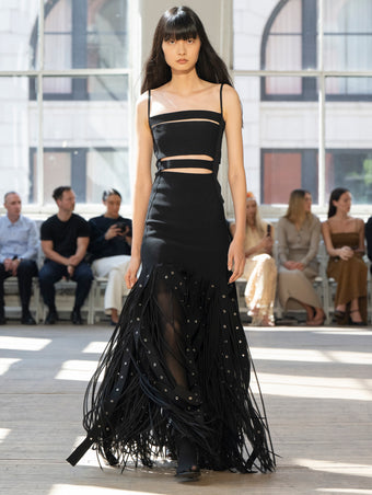 Image of model walking Proenza Schouler SS25 Runway wearing Effe Dress in Compact Viscose Knit in Black and Claudia Skirt in Silk Organza Fringe in Black and Slash Tie Sandal in BLACK