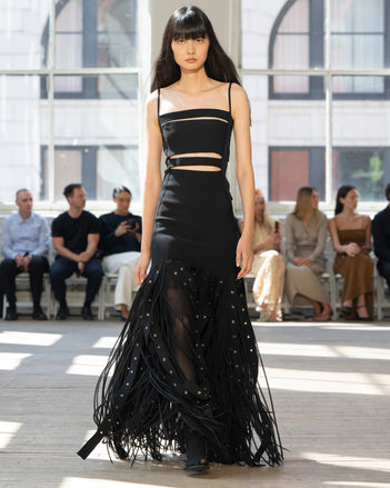 Image of model walking Proenza Schouler SS25 Runway wearing Effe Dress in Compact Viscose Knit in Black and Claudia Skirt in Silk Organza Fringe in Black and Slash Tie Sandal in BLACK