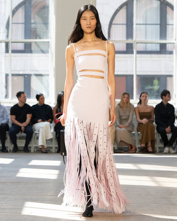 Image of model walking Proenza Schouler SS25 Runway wearing Effe Dress in Compact Viscose Knit in Iris and Claudia Skirt in Silk Organza Fringe in Iris and Silo Bag in Black Satin in BLACK and Slash Tie Sandal in BLACK