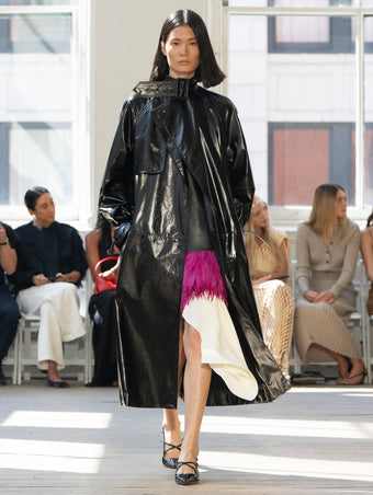 Image of model walking Proenza Schouler SS25 Runway wearing Sabina Coat in Lacquered Leather in Black and Renne Top in Textured Leather in Black and Mali Skirt in Feather Embroidery in Fuschia and Slash Slingback Pump in BLACK
