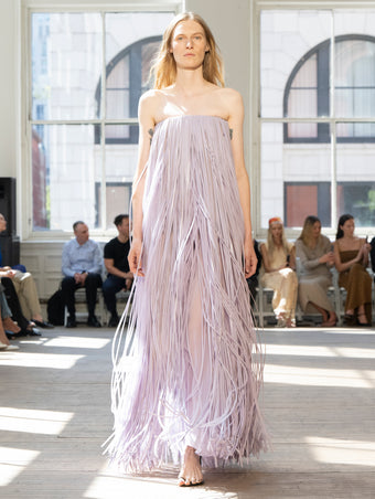 Image of model walking Proenza Schouler SS25 Runway wearing Phia Dress in Leather Silk Fringe in Lavender and Slash Tie Sandal in BLACK