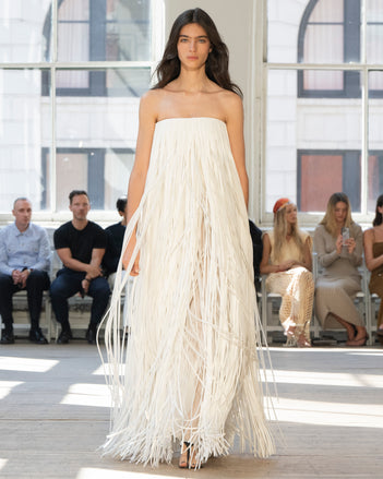 Image of model walking Proenza Schouler SS25 Runway wearing Phia Dress in Leather Silk Fringe in Ecru and Tee Thong Sandal in BLACK