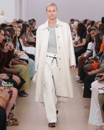 Model Walking Proenza Schouler SS24 Runway In Kiki Tank In White Cotton Mesh, Dara Top In Smoke Technical Nylon Jersey, Ellsworth Jean In Ecru Denim, Billie Coat In Ecru Lacquered Leather, Flip Shoulder Bag In Birch Nappa Leather, Tee Toe Ring Sandals In Black + Cream Nappa Lux