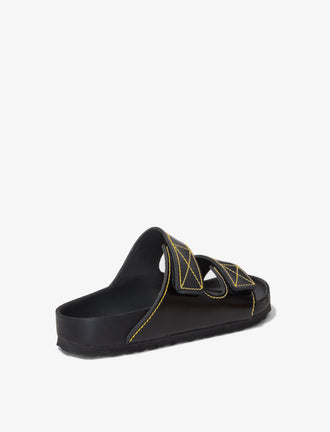 Proenza Schouler back 3/4 image of Birkenstock collaboration Arizona Slides in black with yellow contrast stitching