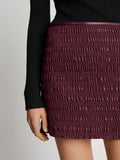 Detail image of model wearing Faux Leather Smocked Mini Skirt in PLUM