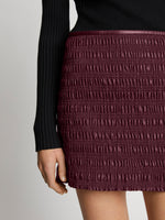 Detail image of model wearing Faux Leather Smocked Mini Skirt in PLUM
