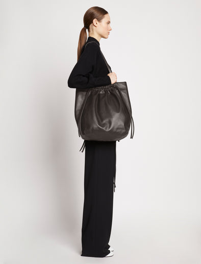 Side image of model carrying Drawstring Tote in DARK CHOCOLATE