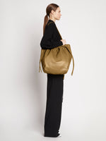 Side image of model carrying Drawstring Tote in TRUFFLE