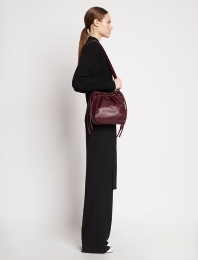 Side image of model carrying Drawstring Pouch in DARK RED