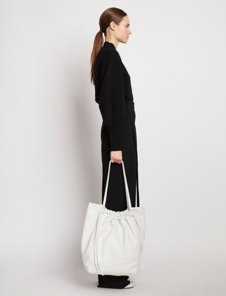 Side image of model carrying Drawstring Tote in OPTIC WHITE