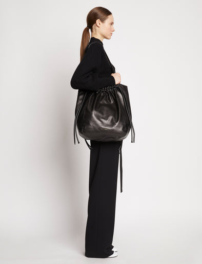 Side image of model carrying Drawstring Tote in BLACK