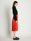 Side full length image of model wearing Faux Leather Pleated Skirt in VERMILLION