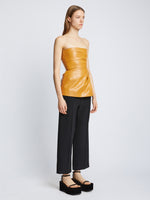 Side full length image of model wearing Glossy Leather Strapless Top in CARAMEL