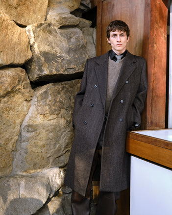 Model wearing Orlando Coat and Charles Sweater standing against a stone wall.