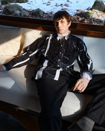Person wearing the black and white garment dyed shirt sitting on a bench with a snowy landscape in the background