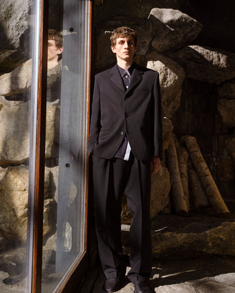Man in a black suit standing in front of a stone wall