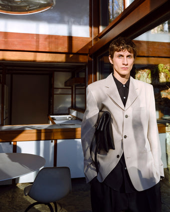 Man in a light gray blazer standing in a modern indoor setting with tables and chairs.