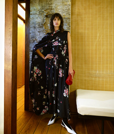 Image of model wearing Ysabelle Dress in Printed Silk Viscose in Black multi holding Silo Clutch in Shiny Calf in Red in an indoor setting