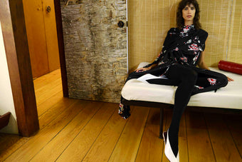 Woman sitting on a white bench in a room with wooden floor and textured walls.
