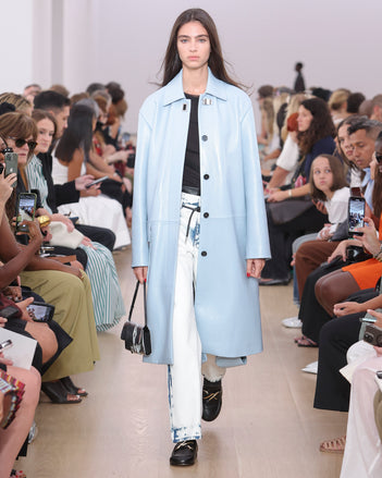 Model Walking Proenza Schouler SS24 Runway In Dara Top In Black Technical Nylon Jersey, Ellsworth Jean In Bleached Denim, Billie Coat In Pale Lapis Lacquered Leather, Flip Shoulder Bag In Silver Metallic Lacquered Nylon, Monogram Loafers In Black Nappa