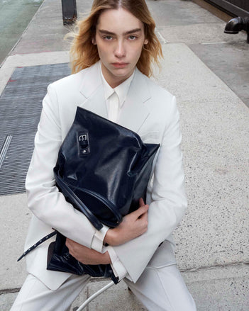 Image of model sitting on the streets holding the Days Carryall in Paper Calf