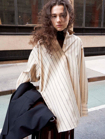 Cropped image of model standing on the sidewalk wearing the Addy Top in Stripe Cotton Silk Poplin in Taupe Multi and the Veda Skirt in Faux Leather Fringe