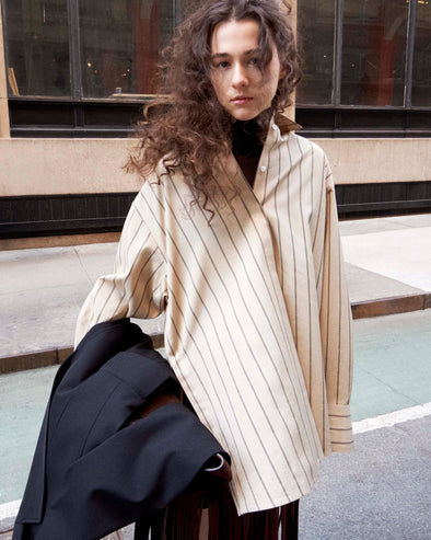 Cropped image of model standing on the sidewalk wearing the Addy Top in Stripe Cotton Silk Poplin in Taupe Multi and the Veda Skirt in Faux Leather Fringe