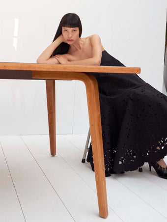 Cropped image of model laying on a table wearing the Olene Skirt in Broderie Anglaise in Black and the Glove Hinge Pumps in Black