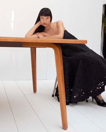 Cropped image of model laying on a table wearing the Olene Skirt in Broderie Anglaise in Black and the Glove Hinge Pumps in Black