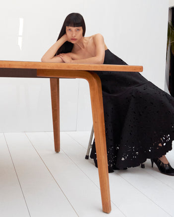 Cropped image of model laying on a table wearing the Olene Skirt in Broderie Anglaise in Black and the Glove Hinge Pumps in Black