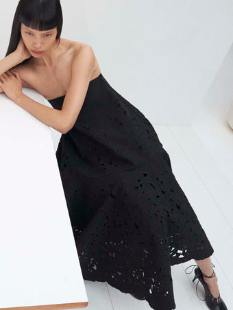 Cropped image of model laying on a table wearing the Olene Skirt in Broderie Anglaise in Black and the Glove Hinge Pumps in Black