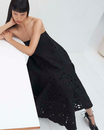 Cropped image of model laying on a table wearing the Olene Skirt in Broderie Anglaise in Black and the Glove Hinge Pumps in Black