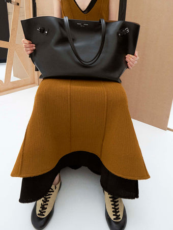 Cropped image of model sitting holding the a bag wearing the Tavia Dress in Viscose Fringe Knit in Olive and the Arcadia Sneakers in Almond holding the Days Carryall in Smooth Calf in Black 