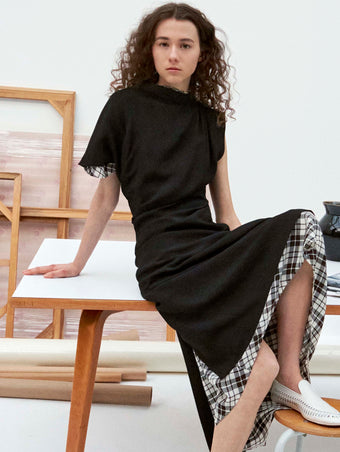 Cropped image of model sitting on table wearing the Hallie Dress in Hammered Viscose in Black, the Hallie Dress in Crinkled Plaid, and the Whip Loafers in Ecru