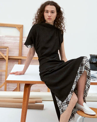 Cropped image of model sitting on table wearing the Hallie Dress in Hammered Viscose in Black, the Hallie Dress in Crinkled Plaid, and the Whip Loafers in Ecru