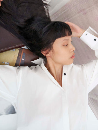 Cropped image of model laying on a table wearing the Addy Shirt in Compact Cotton Poplin 