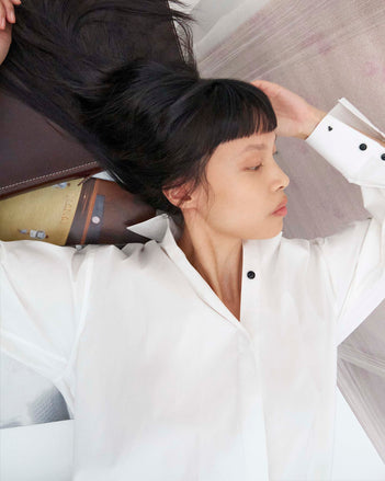 Cropped image of model laying on a table wearing the Addy Shirt in Compact Cotton Poplin 