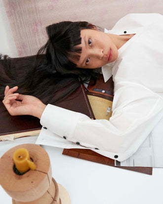 Cropped image of model laying on a table wearing the Addy Shirt in Compact Cotton Poplin 