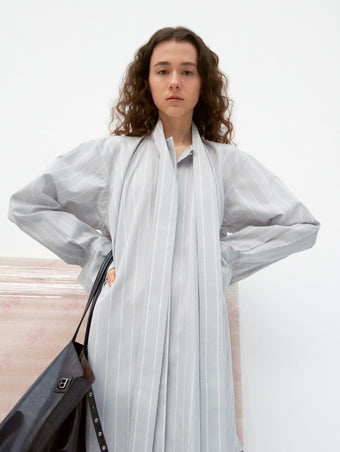 Model standing with hands on her hips wearing Phillipa Dress in Stripe Cotton Silk Poplin in light blue, carrying Days Tote in black