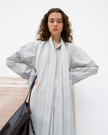 Model standing with hands on her hips wearing Phillipa Dress in Stripe Cotton Silk Poplin in light blue, carrying Days Tote in black